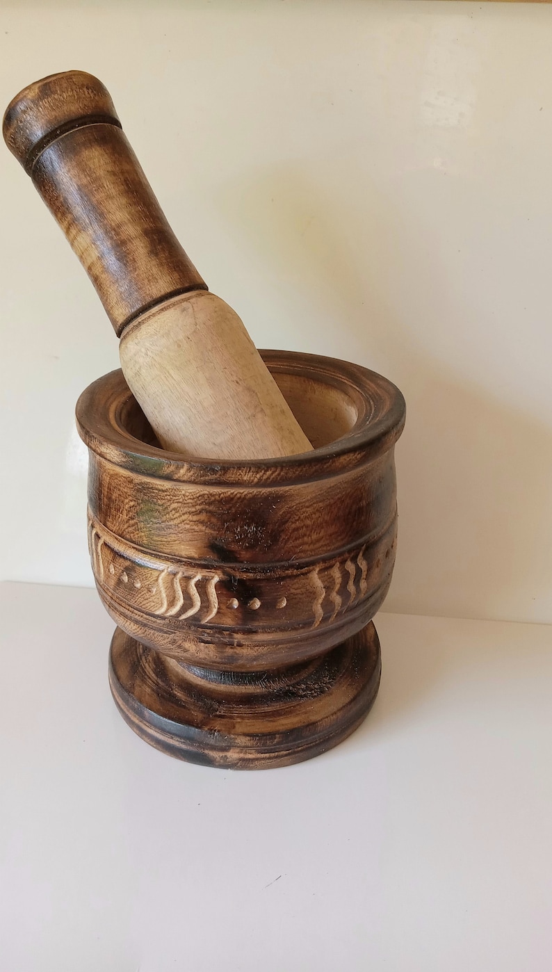 May include: A dark brown wooden mortar and pestle with a carved design. The mortar has a wide base and a deep bowl. The pestle is long and cylindrical.
