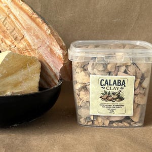 Puede incluir: Un recipiente de pl&aacute;stico transparente lleno de peque&ntilde;os trozos irregulares de arcilla Calaba, con una etiqueta que dice Calaba Clay, 100% natural & unrefined, sun-dried for purity, net weight 1 lb (454 g), junto a un cuenco negro con trozos grandes.