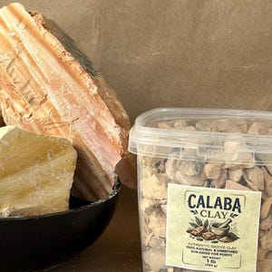 Puede incluir: Un recipiente de pl&aacute;stico transparente lleno de trozos peque&ntilde;os de arcilla Calaba de color tostado, con una etiqueta que incluye '1 lb (454 g)'. Al lado hay un cuenco negro con rocas minerales grandes, estratificadas, naranjas y amarillas.