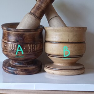 May include: Two wooden mortars and pestles, one with a dark brown finish and the other with a light brown finish. The dark brown mortar has a carved design and the light brown mortar has a simple design. Both mortars have a base and a pestle.