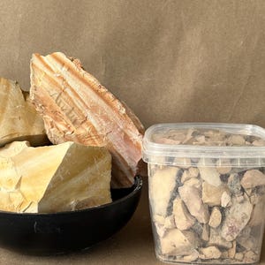 Puede incluir: Un cuenco negro que contiene trozos grandes y dentados de roca sedimentaria de color tostado y crema con capas horizontales visibles, junto a un recipiente de pl&aacute;stico transparente lleno de fragmentos m&aacute;s peque&ntilde;os del mismo material mineral.