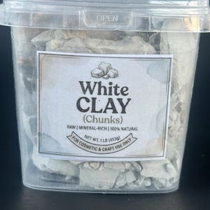 Puede incluir: Un recipiente de plástico transparente lleno de trozos irregulares de arcilla blanca. La etiqueta dice: White CLAY (Chunks), RAW | MINERAL-RICH | 100% NATURAL, NET WT. 1 LB (453g), FOR COSMETIC & CRAFT USE ONLY. La tapa tiene la palabra OPEN.