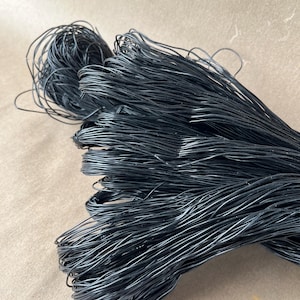 May include: A bundle of thin, flexible black wire arranged in a series of long, parallel strands that curve and loop at the ends. The wire has a smooth, dark finish and is gathered together to form a dense, elongated shape with tangled sections.