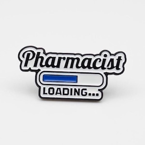 May include: A black and white enamel pin with the word "Pharmacist" above a loading bar graphic. The loading bar is white with a blue progress indicator and the word "LOADING..." below.