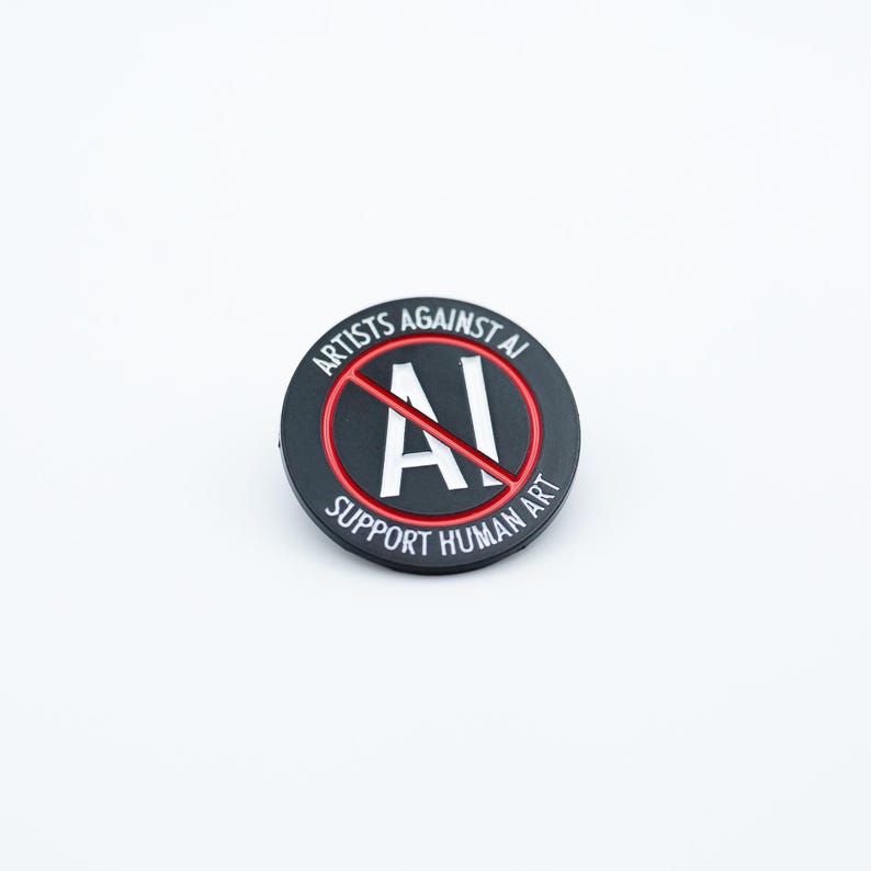 May include: A round, black pin with the text "ARTISTS AGAINST AI" and "SUPPORT HUMAN ART" in white lettering. A red circle with a line through the letters "AI" is in the center. The pin is on a white background.