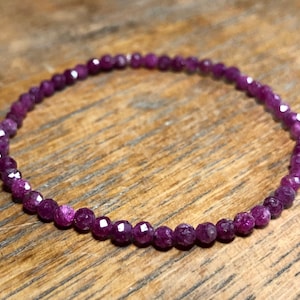 Peut inclure: Un bracelet délicat composé de petites perles de rubis facettées. Le bracelet est de couleur violet foncé et est enfilé sur un cordon élastique transparent.
