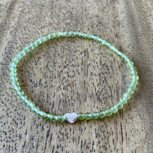 May include: A green peridot gemstone bracelet with a silver heart charm.
