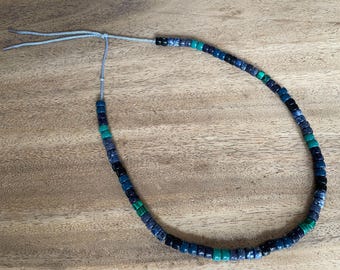 May include: A necklace made of blue, green, and black beads with a gray cord.