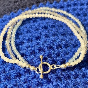 Peut inclure: Un bracelet délicat en perles blanches et bleu clair avec un fermoir à glissière argenté.