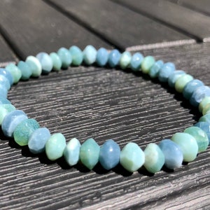 May include: A bracelet made of light blue and green gemstone beads. The beads are faceted and have a slightly iridescent sheen.