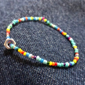 May include: A colourful beaded bracelet with a silver nut clasp. The beads are in shades of blue, green, yellow, orange, red, and purple.