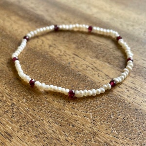 May include: A white pearl bracelet with red gemstone accents.