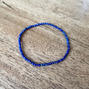 May include: A delicate blue gemstone bracelet made with small, round beads. The bracelet is made with natural lapis lazuli stones.