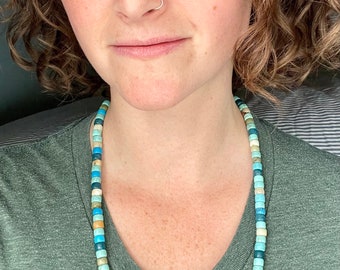 May include: A close-up of a person wearing a green t-shirt and a necklace made of turquoise, blue, and brown beads.