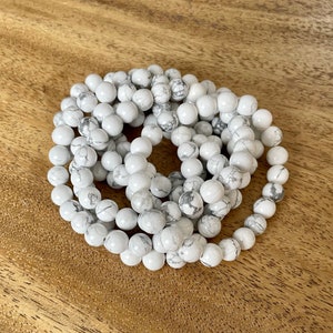 Puede incluir: Un brazalete de cuentas de howlite blancas. El brazalete est&aacute; hecho de cuentas redondas blancas con vetas grises. Las cuentas est&aacute;n enhebradas en un cord&oacute;n el&aacute;stico transparente.