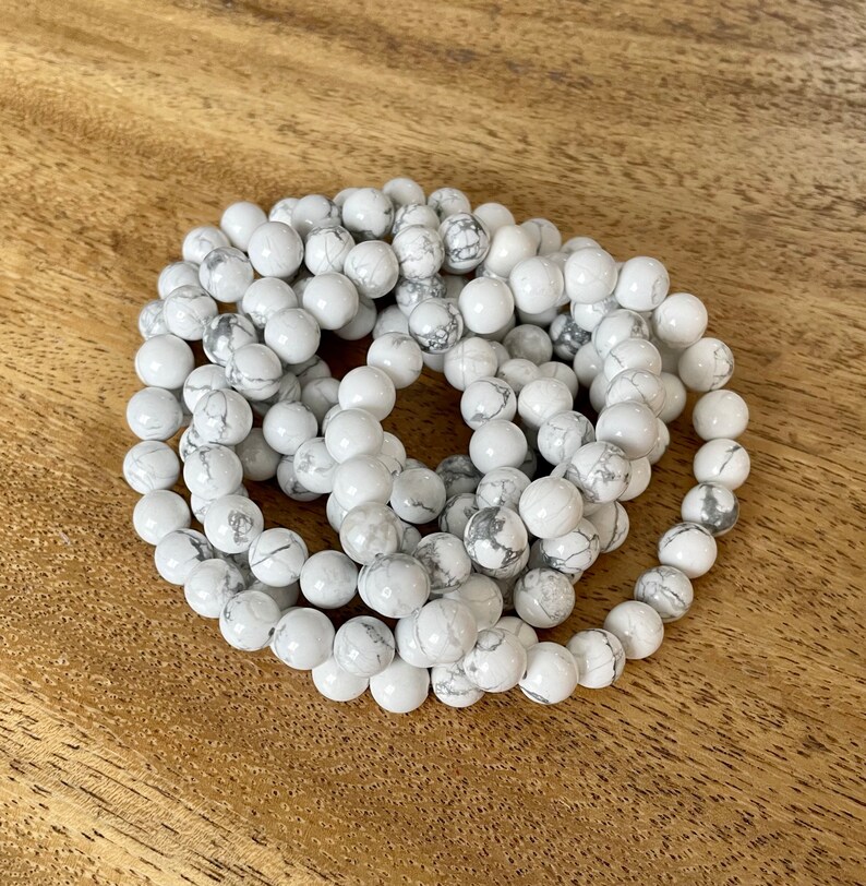 Puede incluir: Un brazalete de cuentas de howlite blancas. El brazalete est&aacute; hecho de cuentas redondas blancas con vetas grises. Las cuentas est&aacute;n enhebradas en un cord&oacute;n el&aacute;stico transparente.