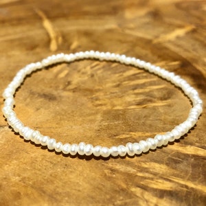 May include: A white pearl bracelet with small, evenly spaced pearls.