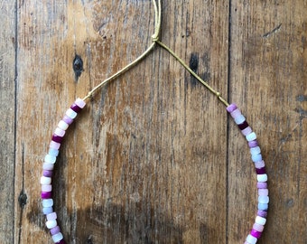 May include: A necklace made of small, square-shaped beads in shades of pink, purple, and white. The necklace is strung on a gold cord.