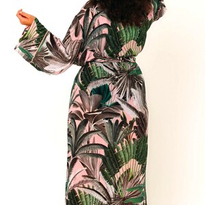 Puede incluir: Una bata larga de color rosa y verde con estampado de hojas tropicales. La bata tiene un cintur&oacute;n de atar y mangas largas.