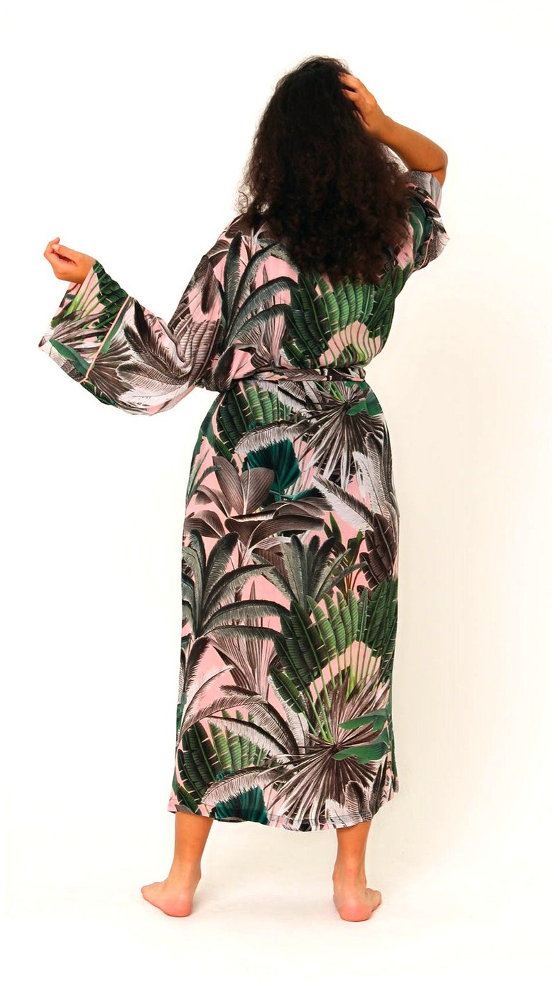 Puede incluir: Una bata larga de color rosa y verde con estampado de hojas tropicales. La bata tiene un cintur&oacute;n de atar y mangas largas.
