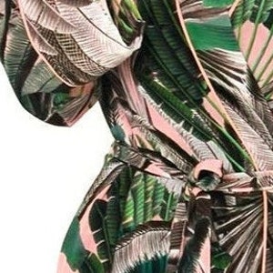 Puede incluir: Una bata de color rosa y verde con estampado tropical y una cinta para atar. La bata tiene manga larga y cuello en V.