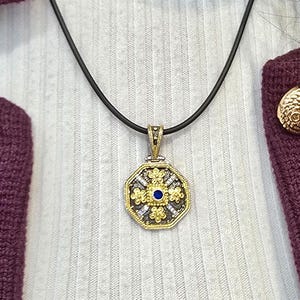 Octagonal silver and gold pendant featuring a central blue cubic zirconia surrounded by four rows of clear cubic zirconia and gold floral motifs