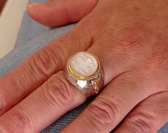 May include: A silver ring with a white stone set in a gold bezel. The ring has a textured band and is worn on a finger.