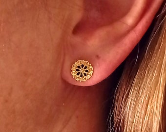 May include: A pair of gold earrings with a delicate, intricate design. The earrings are small and round, and they have a floral pattern.