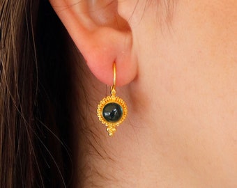 Peut inclure: Boucles d'oreilles créoles en or avec une pierre précieuse vert foncé sertie dans un sertissage en or. Les boucles d'oreilles ont un design délicat avec de petites perles dorées autour de la pierre précieuse.