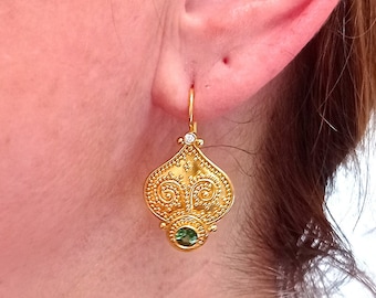Peut inclure: Boucles d'oreilles pendantes en or avec une pierre précieuse verte et un motif de filigrane complexe. Les boucles d'oreilles sont présentées sur l'oreille d'une personne.