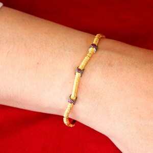 May include: A gold bracelet with a delicate chain design and small red gemstones. The bracelet is on a person's wrist.