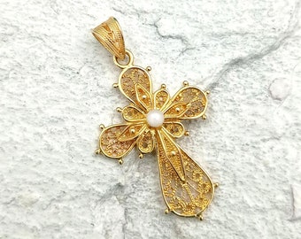 May include: A gold filigree cross pendant with a small white pearl in the center. The pendant is on a white background.