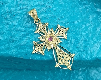 May include: A gold filigree cross pendant with a pink gemstone in the center. The cross is on a turquoise background.