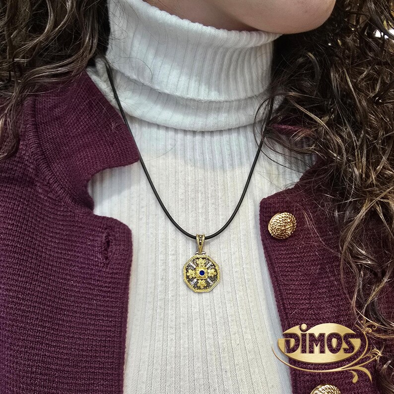 Octagonal silver and gold pendant featuring a central blue cubic zirconia surrounded by four rows of clear cubic zirconia and gold floral motifs