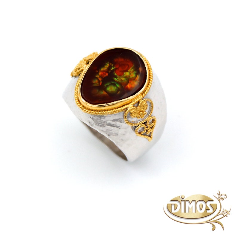 May include: A silver ring featuring a large, oval-shaped, multi-coloured agate gemstone set in a gold bezel. The ring has a textured band and intricate gold detailing.