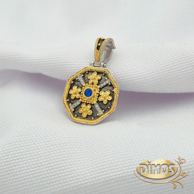 Octagonal silver and gold pendant featuring a central blue cubic zirconia surrounded by four rows of clear cubic zirconia and gold floral motifs