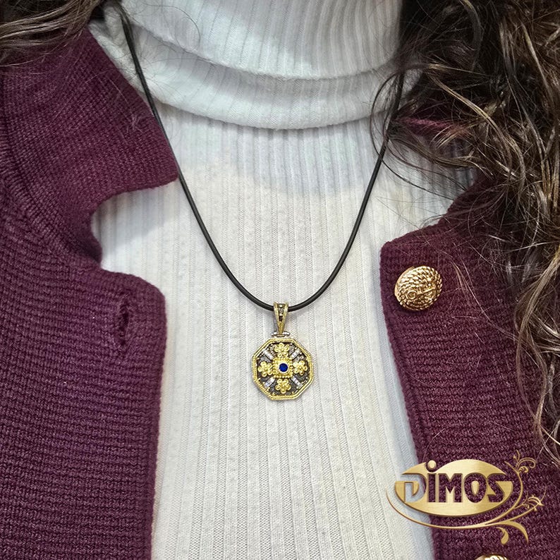 Octagonal silver and gold pendant featuring a central blue cubic zirconia surrounded by four rows of clear cubic zirconia and gold floral motifs