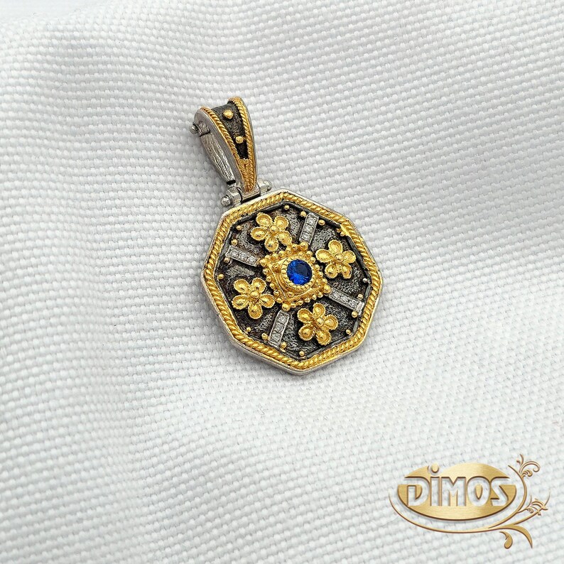 Octagonal silver and gold pendant featuring a central blue cubic zirconia surrounded by four rows of clear cubic zirconia and gold floral motifs