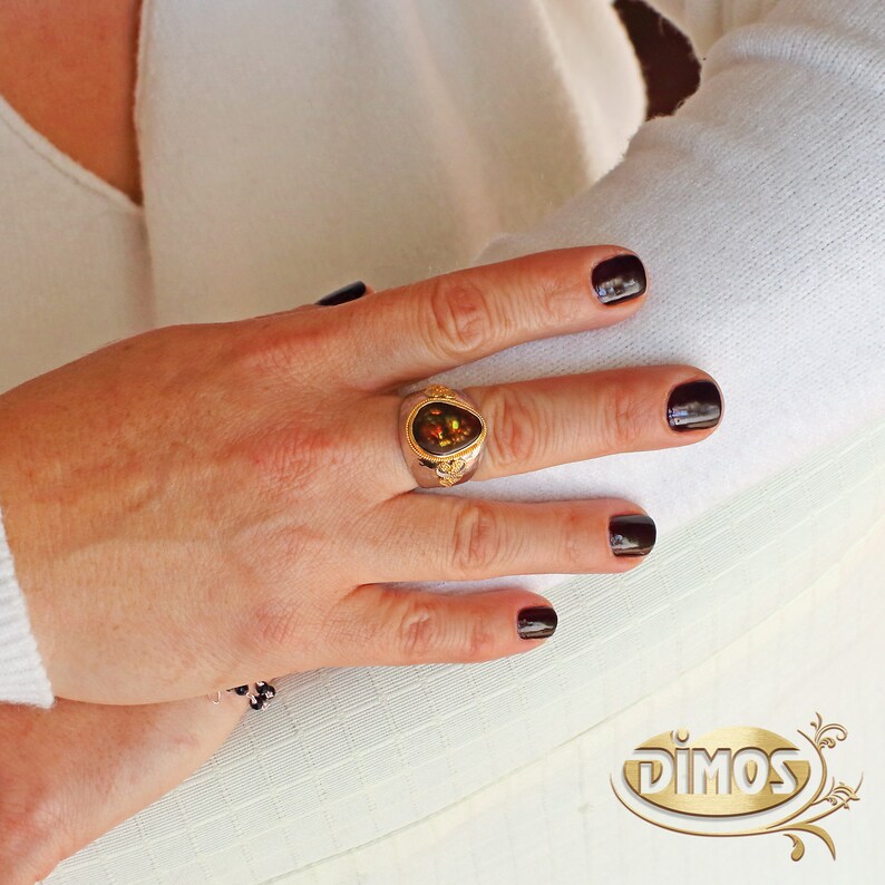 May include: A gold ring with a teardrop-shaped brown gemstone set in a silver band. The ring is on a person's finger.