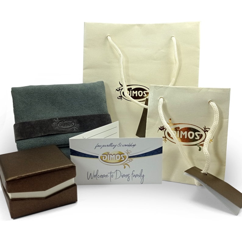 May include: An assortment of jewelry packaging and accessories. Includes two cream-colored shopping bags with white rope handles, a gray polishing cloth with a dark brown band, a brown jewelry box, and a business card with the text "Welcome to Dimos family."