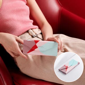 Może przedstawiać: Koperta z geometrycznym wzorem w odcieniach różu, czerwieni i turkusu. Na przodzie nadrukowano napis "SUPPEAL". Koperta jest trzymana przez osobę.