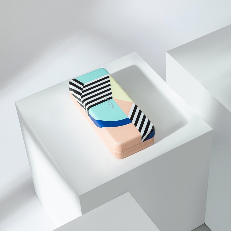 May include: A rectangular case with a colorful geometric design. The case features a pastel peach base, with sections of light blue, yellow, and blue. Black and white stripes accent the top. The word "APPEAL" is printed on the case.