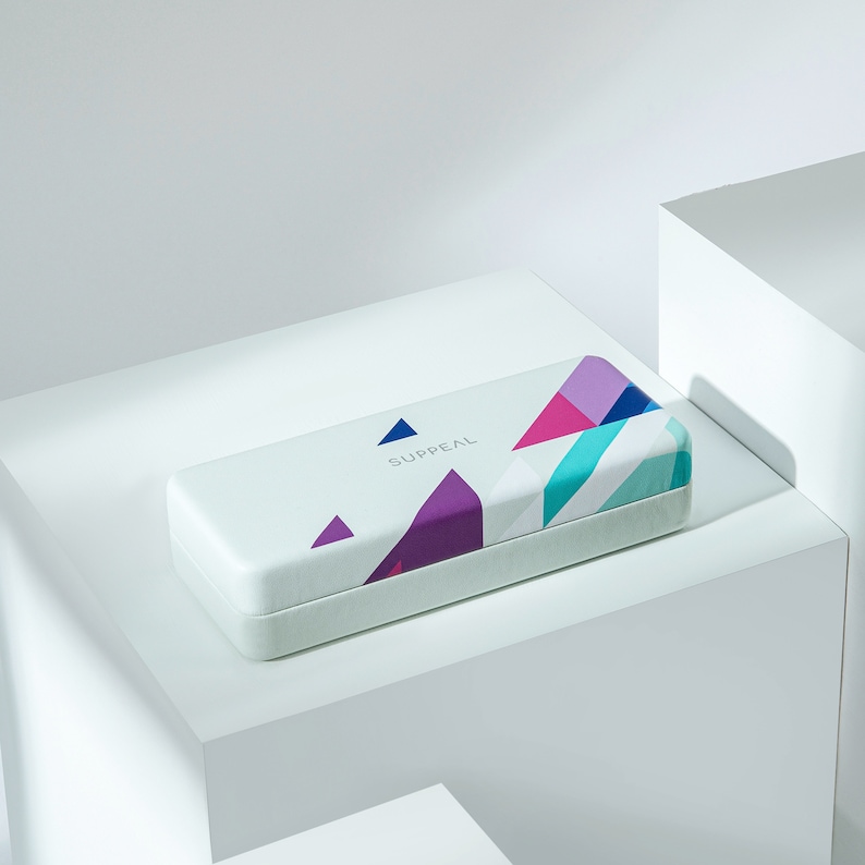 May include: A rectangular, white case with the word "SUPPEAL" printed on the top. The case features a geometric design with triangles in shades of purple, pink, teal, and blue. The case is resting on a white surface.