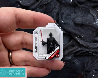 May include: A Kylo Ren action figure from Star Wars in a clear plastic package. The figure is black and holds a red lightsaber. The package has the Star Wars Toybox logo and the number 13.