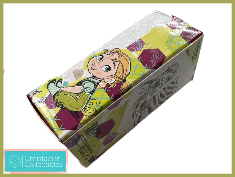 May include: A rectangular box featuring a cartoon image of a young girl with blonde hair and a green dress. The box has a yellow, maroon, and white geometric pattern. The box is labeled "Christacilin Collectibles".