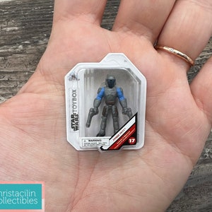 May include: A Star Wars Toybox figure of Jango Fett in a clear plastic package. The figure is gray with blue accents and holds two blasters. The package has the Star Wars Toybox logo and the number 17.