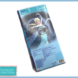 Pu&ograve; includere: Una scatola rettangolare blu con Elsa di Frozen della Disney. La scatola presenta un'immagine di Elsa con un abito fluente. Il testo "Elsa" &egrave; visibile, insieme ad altro testo in pi&ugrave; lingue. La scatola &egrave; leggermente angolata.