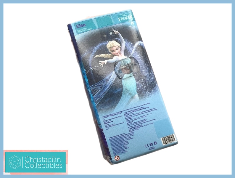 Pu&ograve; includere: Una scatola rettangolare blu con Elsa di Frozen della Disney. La scatola presenta un'immagine di Elsa con un abito fluente. Il testo "Elsa" &egrave; visibile, insieme ad altro testo in pi&ugrave; lingue. La scatola &egrave; leggermente angolata.