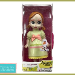 May include: A Disney Animators' Collection Anna doll in a clear plastic display case. The doll wears a light green dress with a pink bow and holds a small Olaf figure. The packaging includes the Disney Animators' Collection logo.