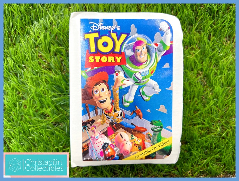 May include: A vintage Disney's Toy Story VHS tape. The cover features Woody, Buzz Lightyear, and other characters against a blue sky background. The title is in yellow and red. The tape is on a green surface.